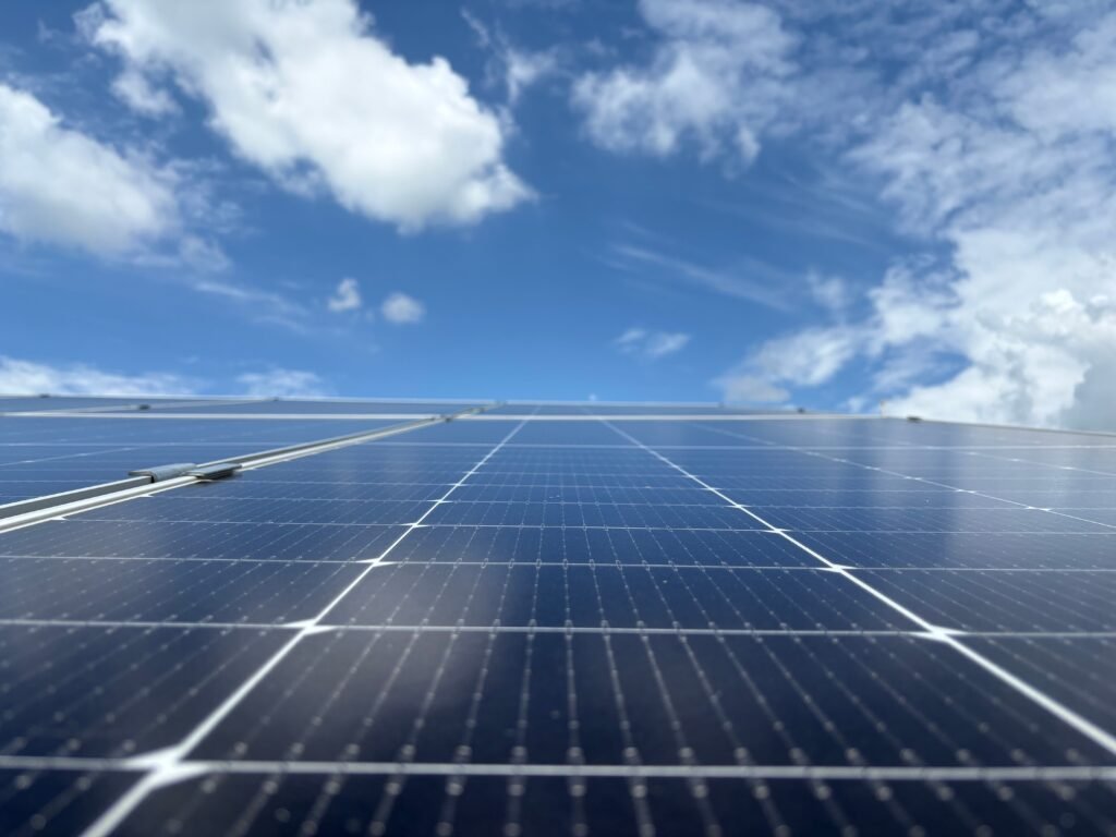 Close-up of solar panels with a clear blue sky and fluffy clouds in Dehradun, India.